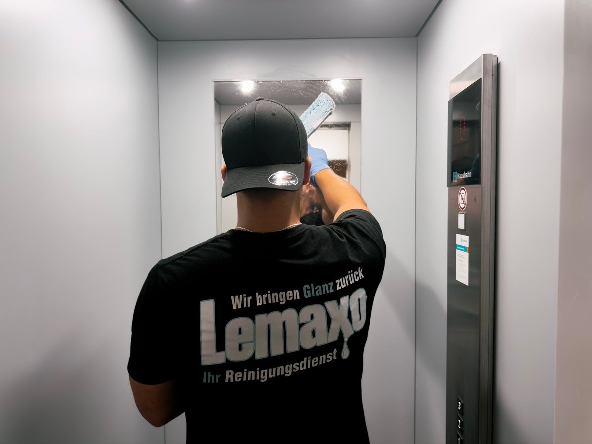 Worker in Lemaxo uniform adjusting black cap in elevator, taking selfie with phone